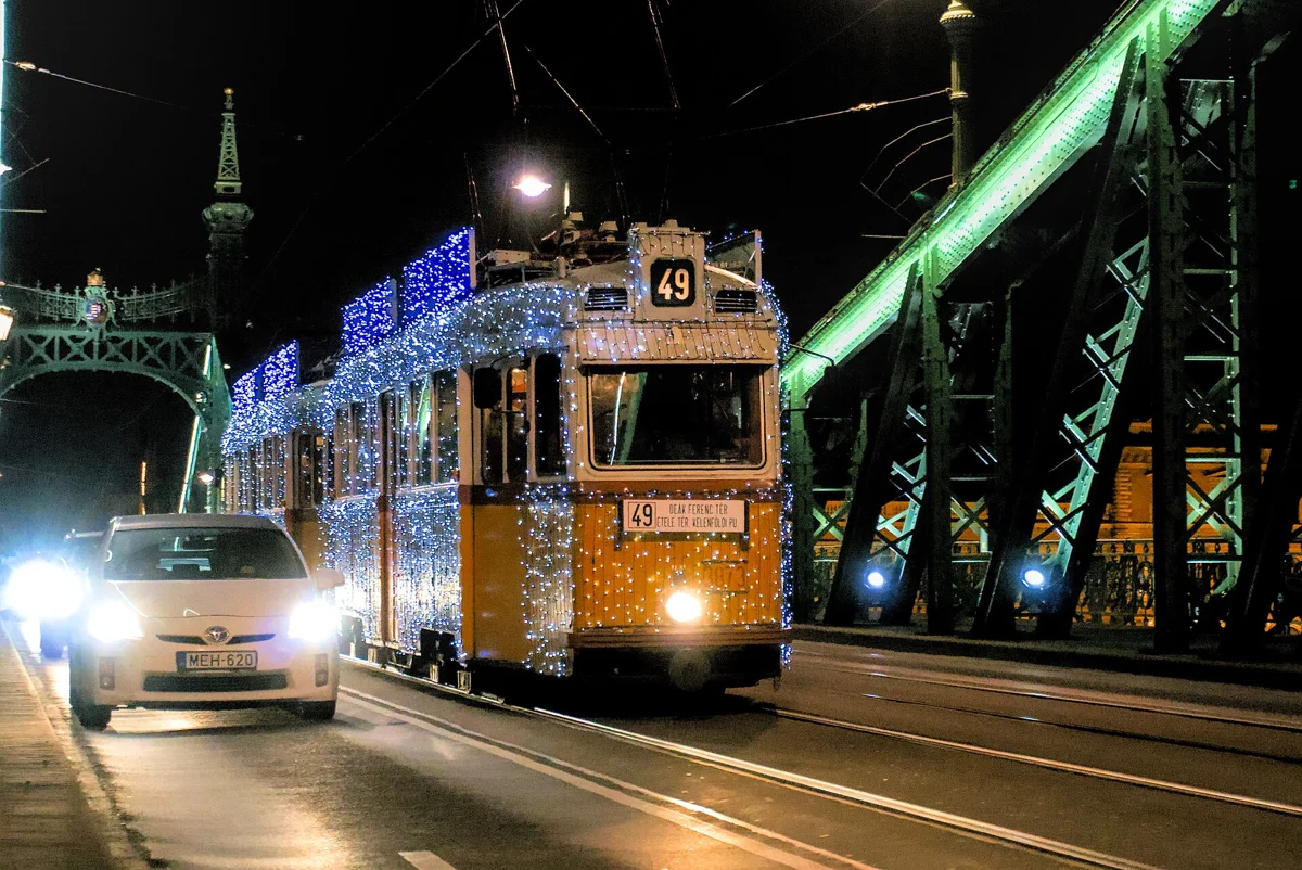 A tram covered in Christmas lights crossing Liberty Bridge, a sight on the evening of a Budapest Christmas market tour